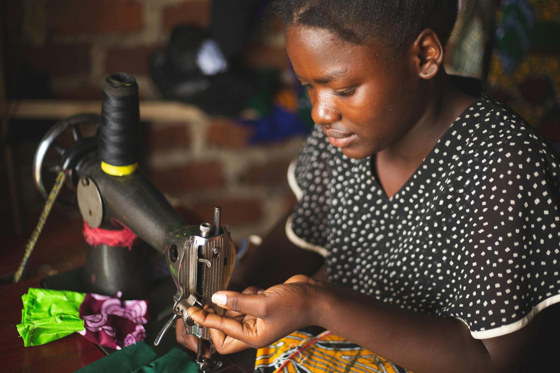 A young seamstress at her sewing machine, threading the needle by hand.